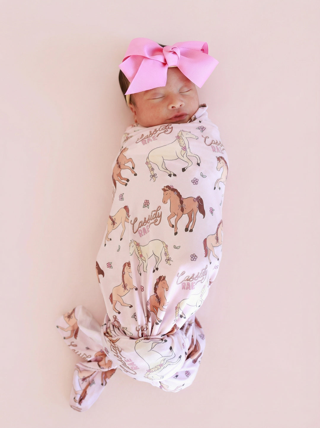 sleeping newborn girl in pony club pink personalized swaddle blanket with matching pink ribbon bow headband