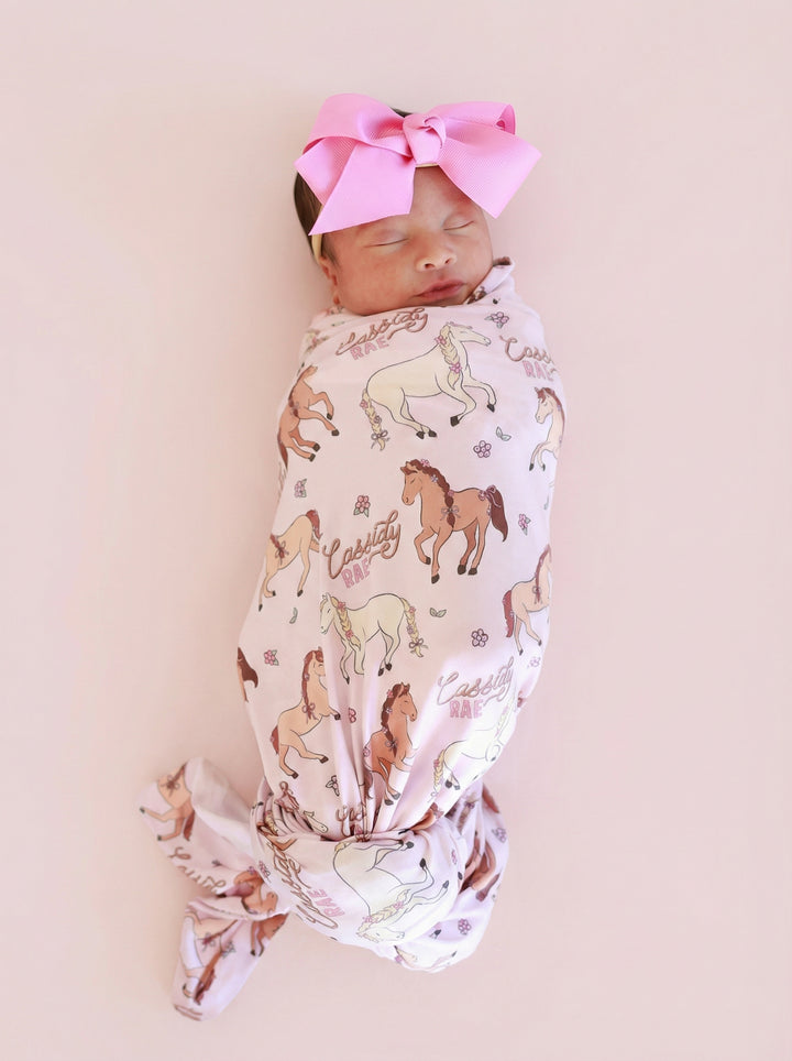 sleeping newborn girl in pony club pink personalized swaddle blanket with matching pink ribbon bow headband