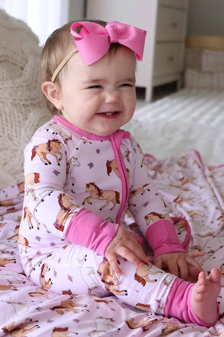 smiling baby girl in pony club pink convertible zip romper with hot pink ribbon bow headband 