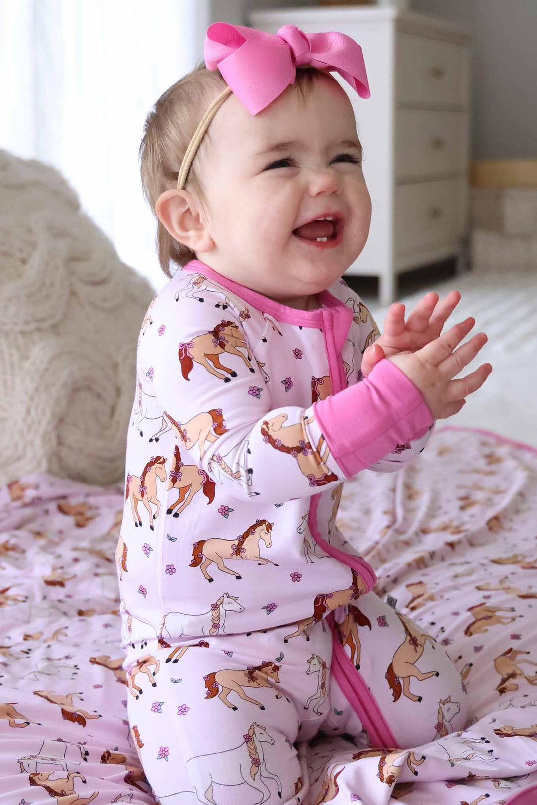 kneeling baby girl wearing pony club pink convertible zip romper with matching ribbon bow headband clapping her hands 