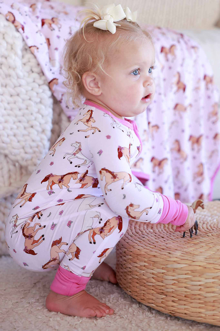 baby girl bending down wearing the pony club pink convertible zip romper pajama with hot pink cuffs