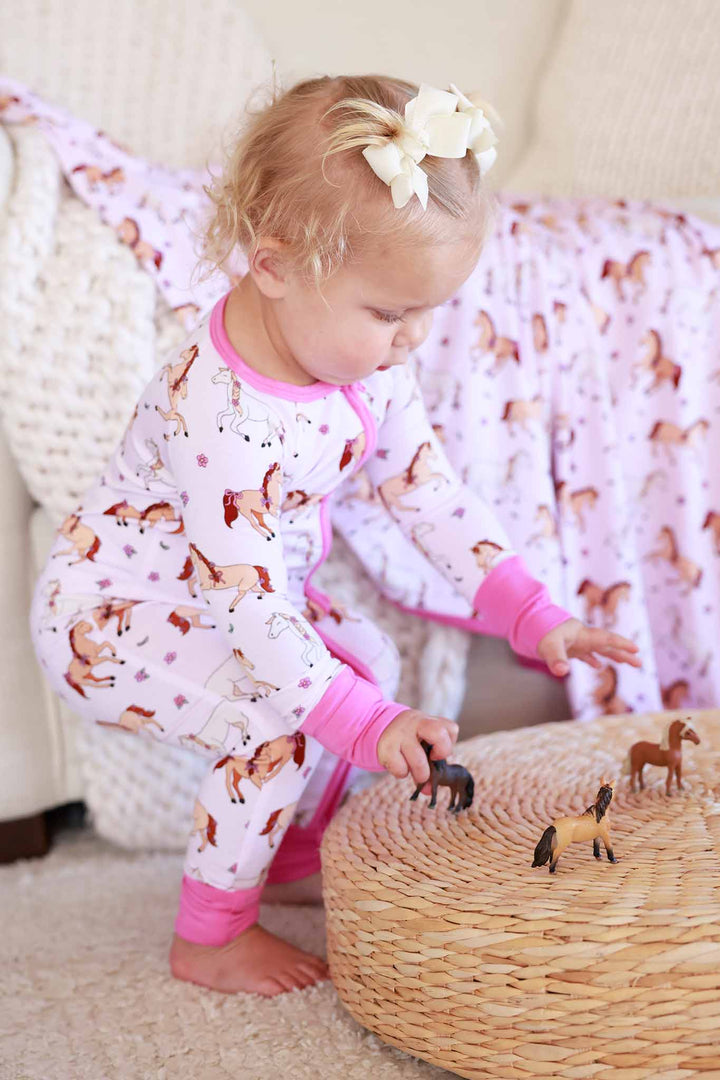 baby girl playing with toy horses wearing a girly pink horse convertible zip romper 