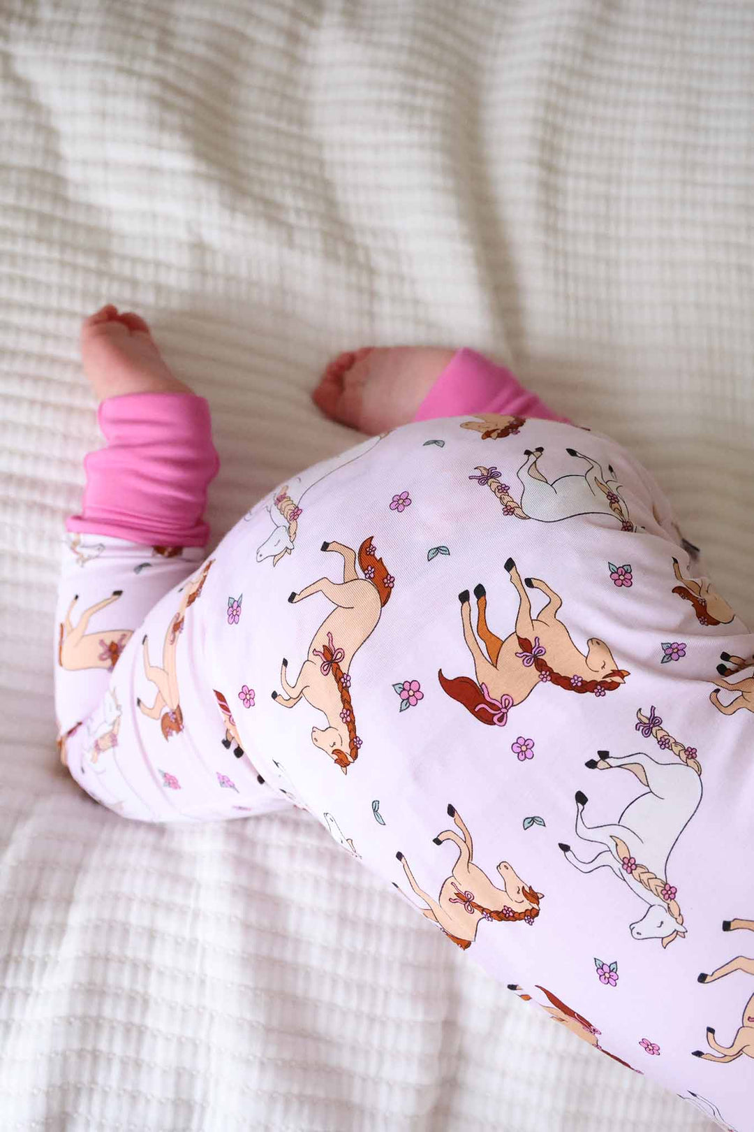 top view of crawling baby girl wearing the pony club pink convertible zip romper 