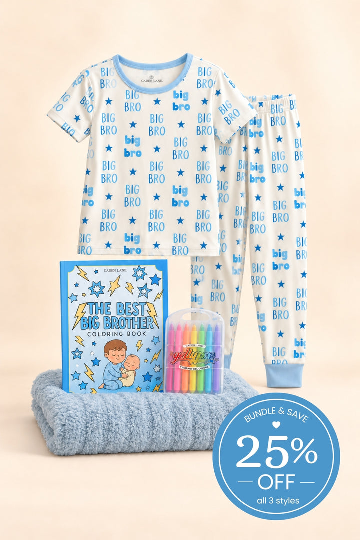 Product shot of a Caden Lane blue bamboo short-sleeve pajama set in a Big Bro print featuring blue lettering and stars, paired with a coloring book, crayons and slate blanket.