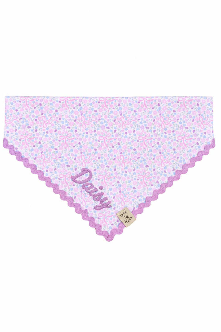 Embroidered pet bandana in the Ribbon Garden print — soft pink and lavender floral fabric with a purple scalloped embroidered edge — displayed flat in a triangle shape, personalized with the name "Daisy"