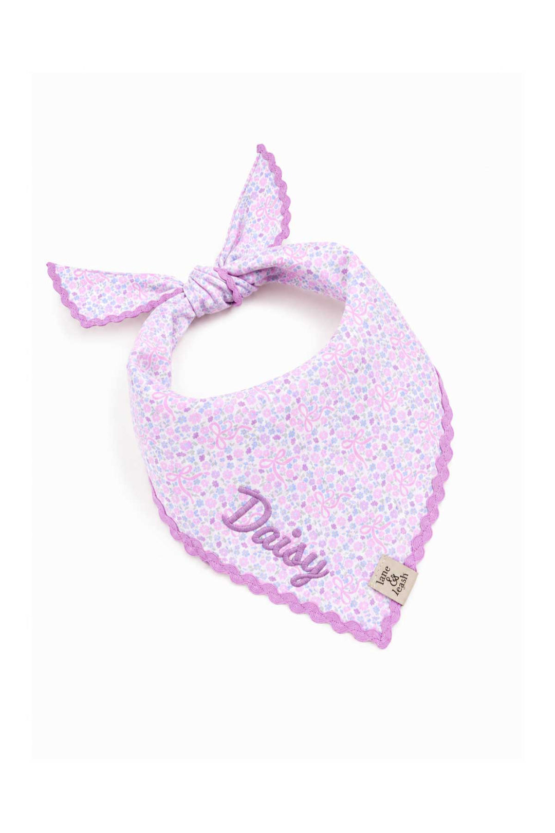 Embroidered pet bandana in the Ribbon Garden print tied in a bow, featuring a purple scalloped embroidered edge, personalized with the name "Daisy"