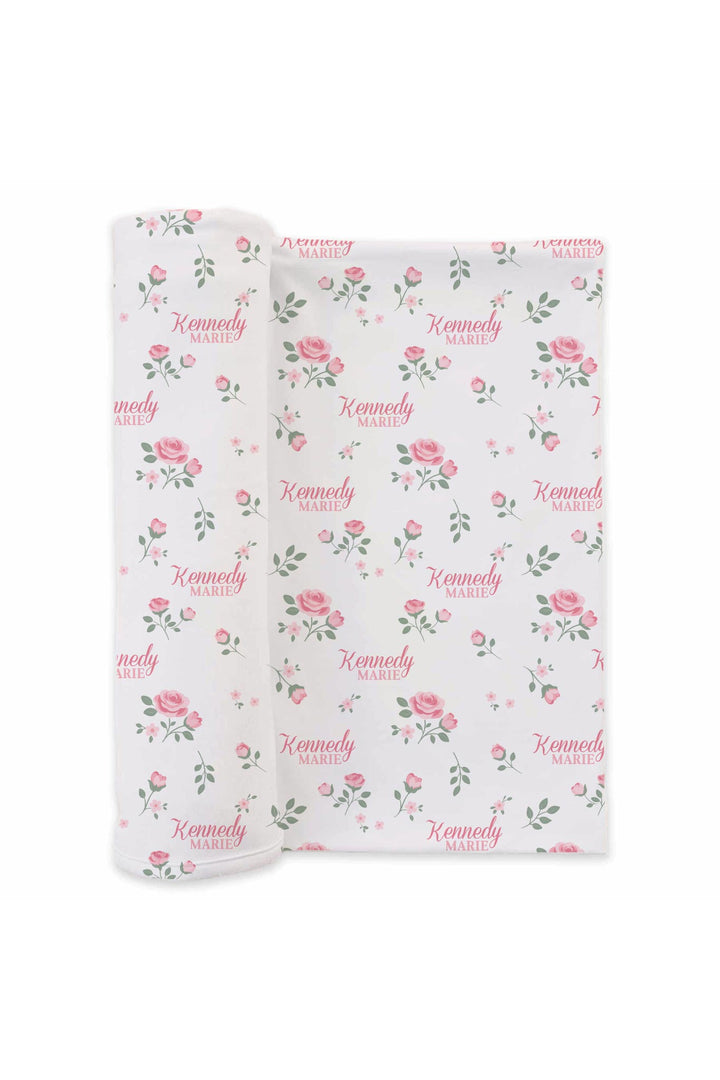 Caden Lane personalized baby swaddle blanket, Rose Garden White floral pattern with custom name, folded and rolled