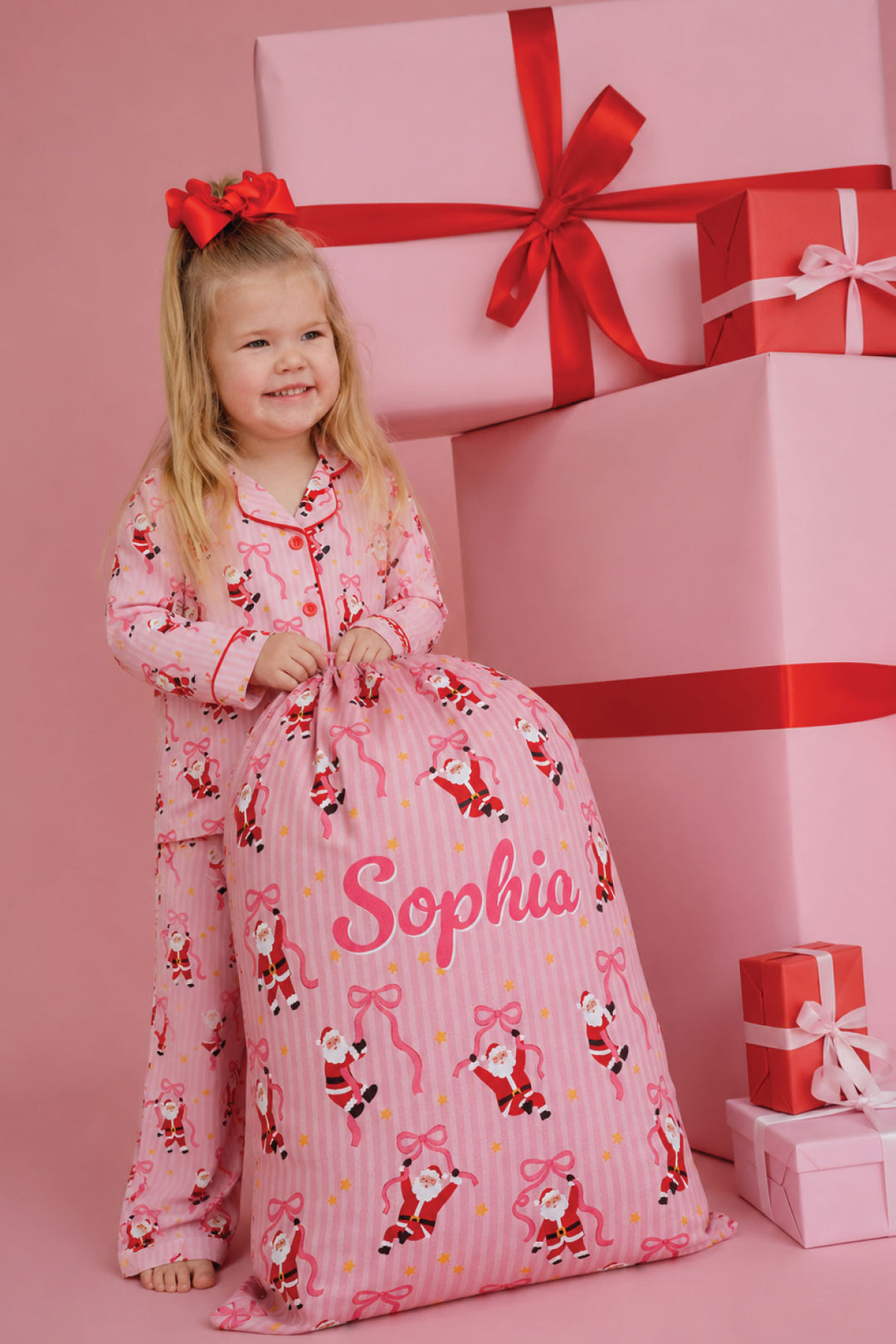 Child wearing Caden Lane Jolly Ribbons Christmas pajamas holding a personalized Christmas Santa Sack, matching festive holiday pajamas, personalized gifts, and Christmas accessories