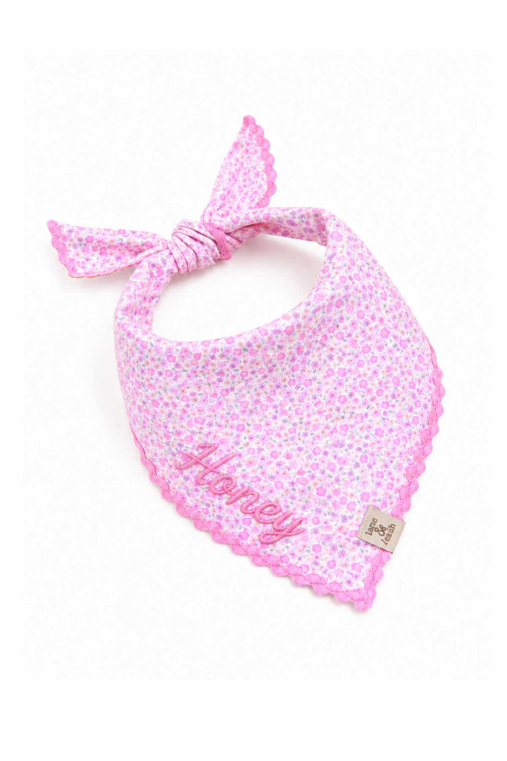 Embroidered pet bandana tied in a bow knot, featuring Scattered Blooms pink floral print, pink ric-rac trim, and embroidered pet name in script