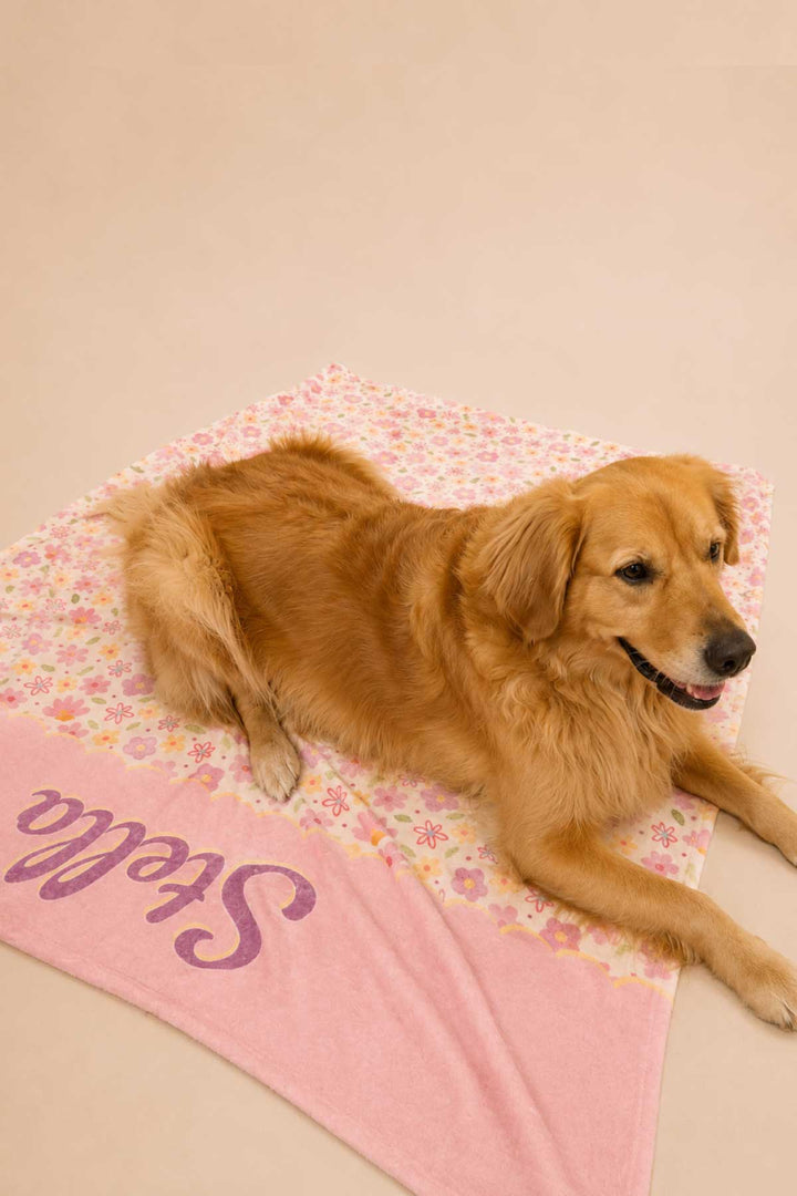 Golden retriever dog lying on a personalized Scattered Blooms pet blanket with pink floral print and pink panel with pet name
