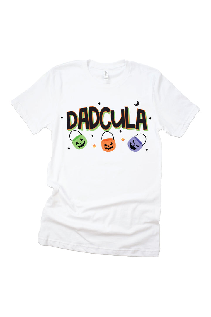 White adult t-shirt with green-outlined black 'DADCULA' lettering, a small crescent moon, and three colorful jack-o-lantern candy bucket icons below