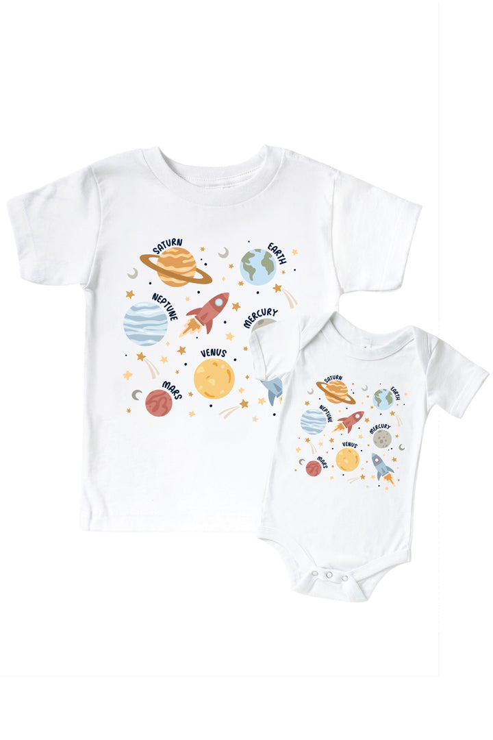 Flat lay of a matching Caden Lane white kids’ tee and bodysuit pair with a Stellar Snuggles graphic featuring a rocket and planets, reading “Nathan.”