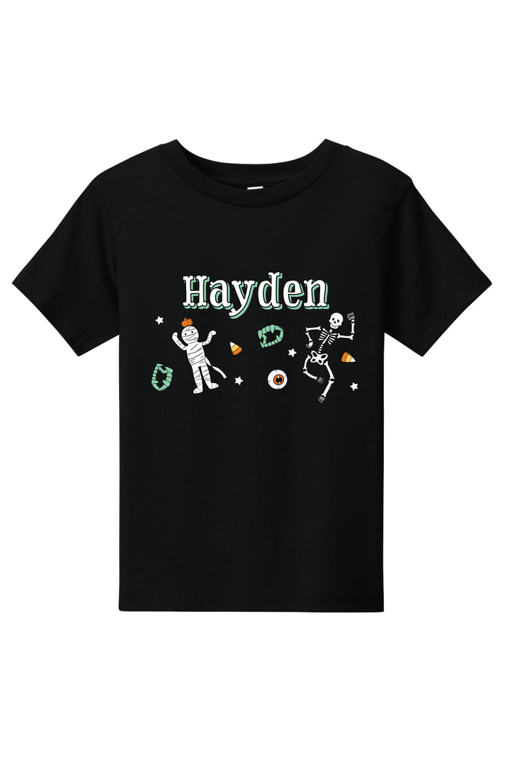 Black kids' T-shirt personalized with the name 'Hayden' and Halloween graphics including dancing skeletons, an eyeball, and candy corn.