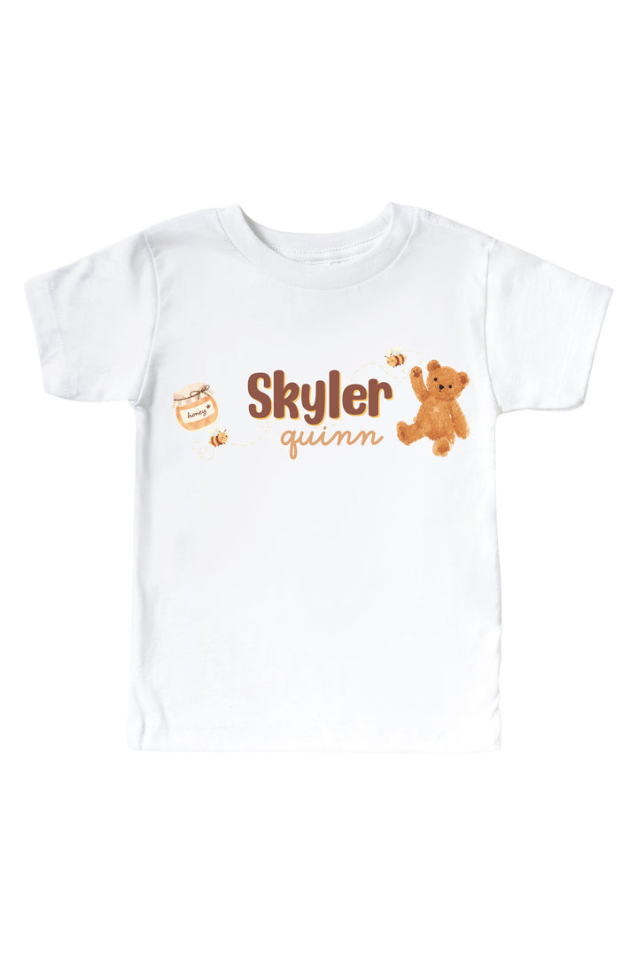 White t-shirt personalized with the name 'Skyler Quinn' alongside a honey jar, bees, and teddy bear graphic, laid flat on a white background