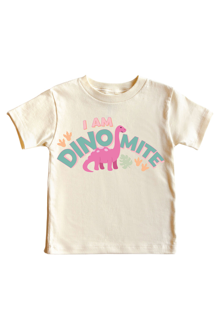 Natural cream kids tee with I AM DINOMITE text in teal and pink lettering featuring a pink brontosaurus dinosaur graphic with colorful leaf accents
