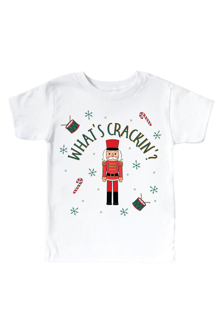 Caden Lane's white "What's Crackin'" toddler t-shirt featuring a red and green toy soldier nutcracker with snowflakes, candy canes, and drums, laid flat.