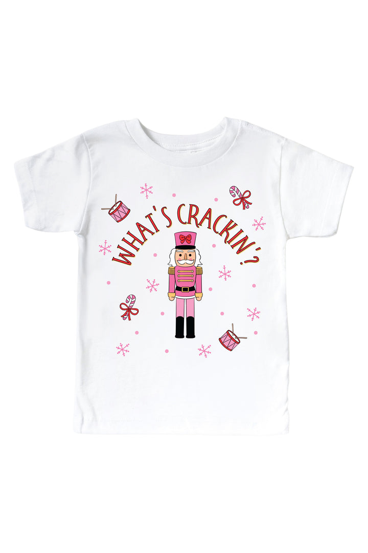 Caden Lane's white "What's Crackin'" toddler t-shirt featuring a pink toy soldier nutcracker with snowflakes, candy canes, and drums, laid flat.