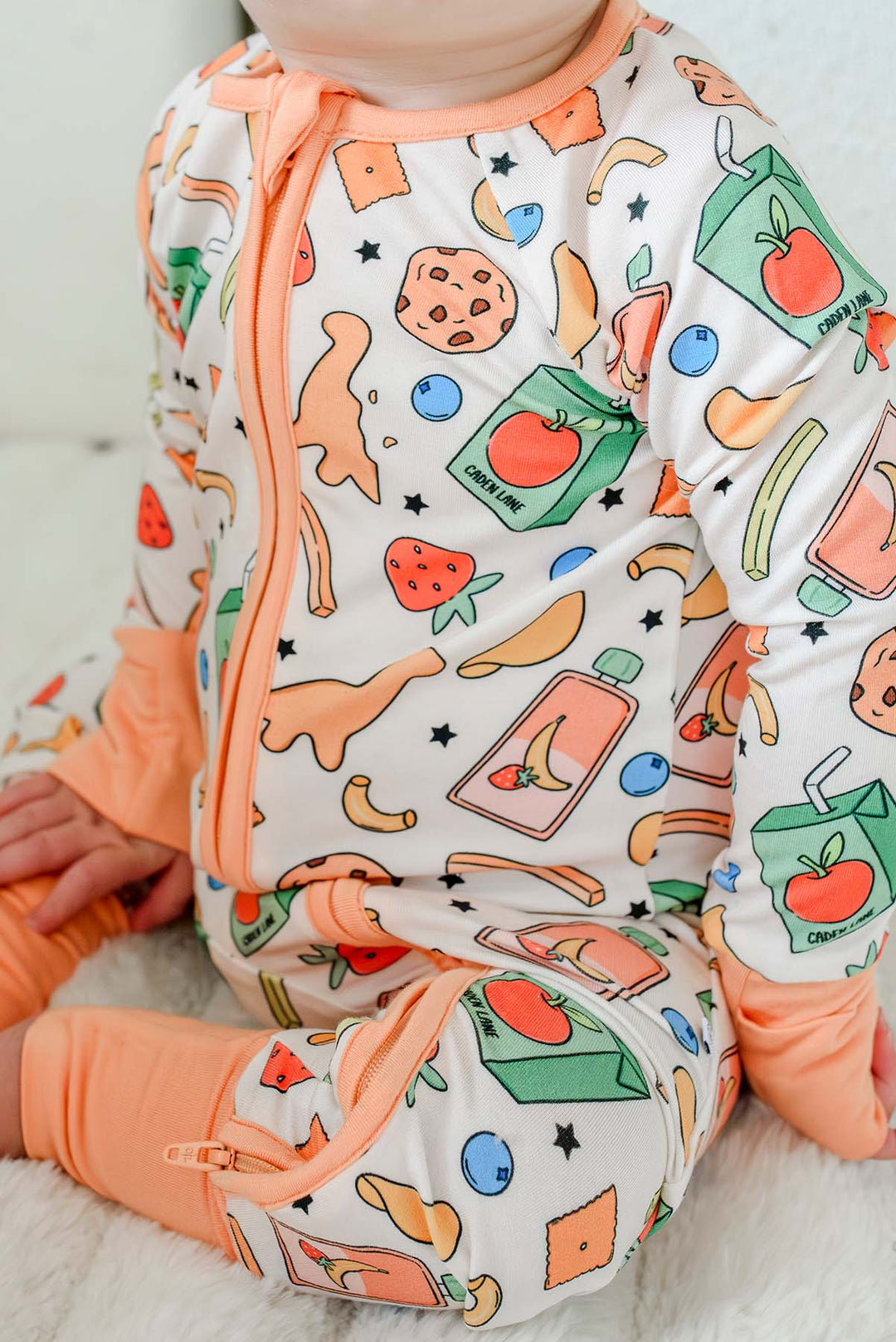 Baby looking down at a chocolate chip cookie while seated in the Snack Attack Convertible Bamboo Zip Romper, with the open-toe cuffs showing the convertible footless styling option