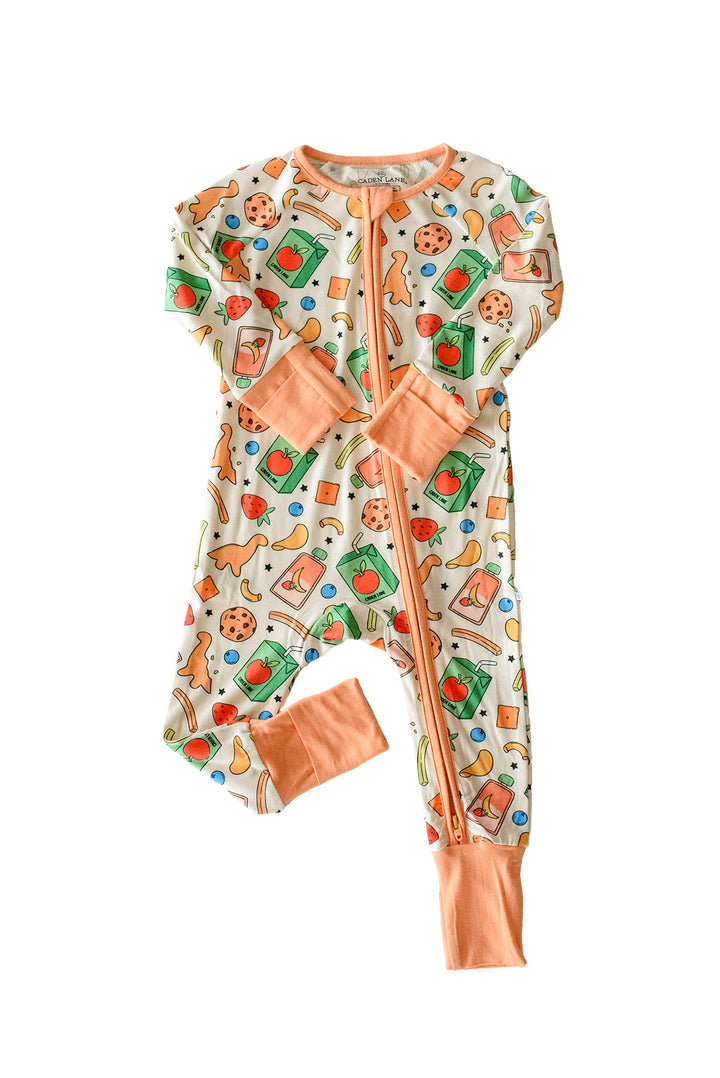 Flat lay of the Snack Attack Convertible Bamboo Zip Romper on a white background, featuring a playful snack-themed print with cookies, strawberries, bananas, green juice cartons, and dinosaur crackers on cream, with peach orange zipper and convertible cuffs