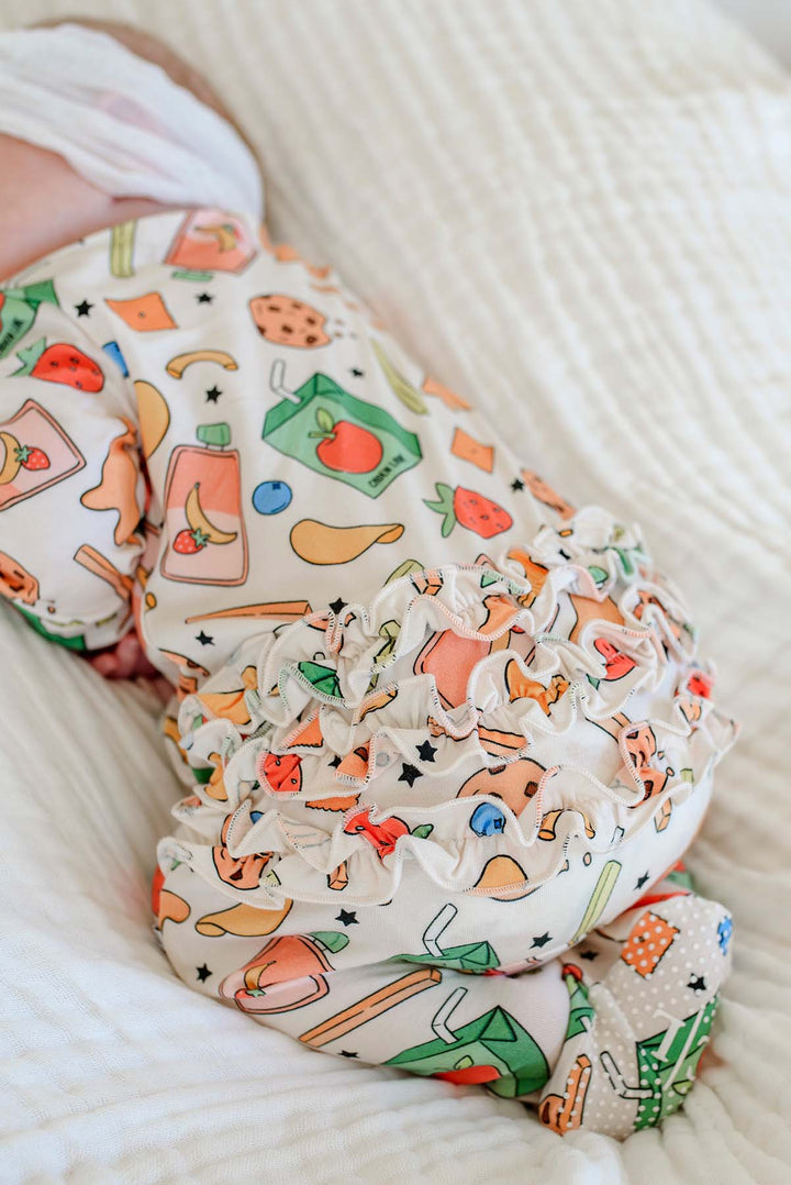 Detailed close-up of a newborn's feet and lower legs in the Snack Attack Ruffle Bamboo Zipper Footie, highlighting the ruffle trim and the snack print with banana juice box, apple juice carton, and playful snack icons
