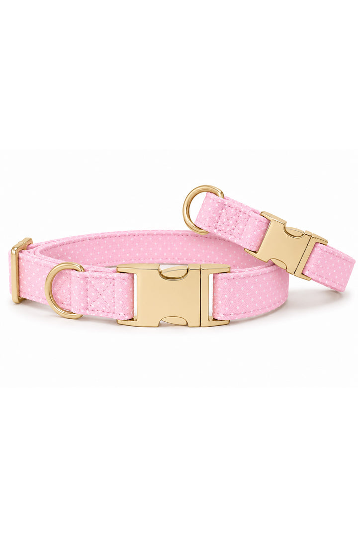 Two pink polka dot dog collars of different sizes stacked together, both featuring gold quick-release buckles and D-rings