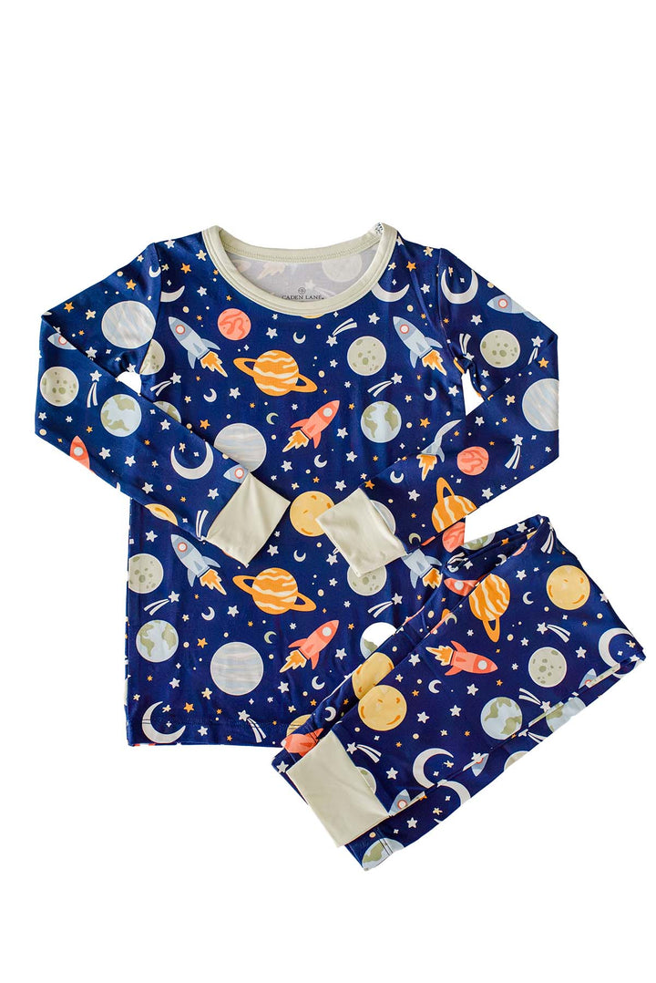 Flat lay of a Caden Lane navy bamboo two-piece pajama set with a long-sleeve top and folded pants in a Stellar Snuggles print featuring planets, rockets, and stars.