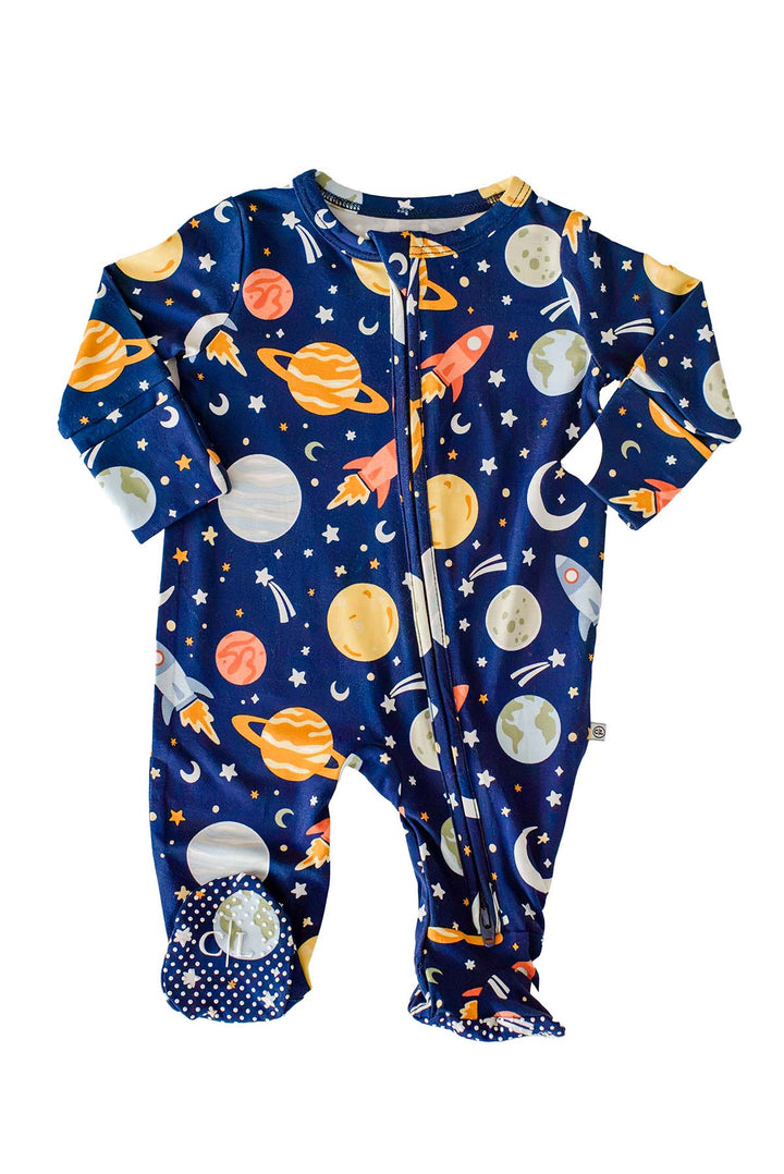 Flat lay of a Caden Lane navy bamboo glow-in-the-dark zipper footie in a Stellar Snuggles print featuring planets, rockets, moons, and stars, shown with arms outstretched.