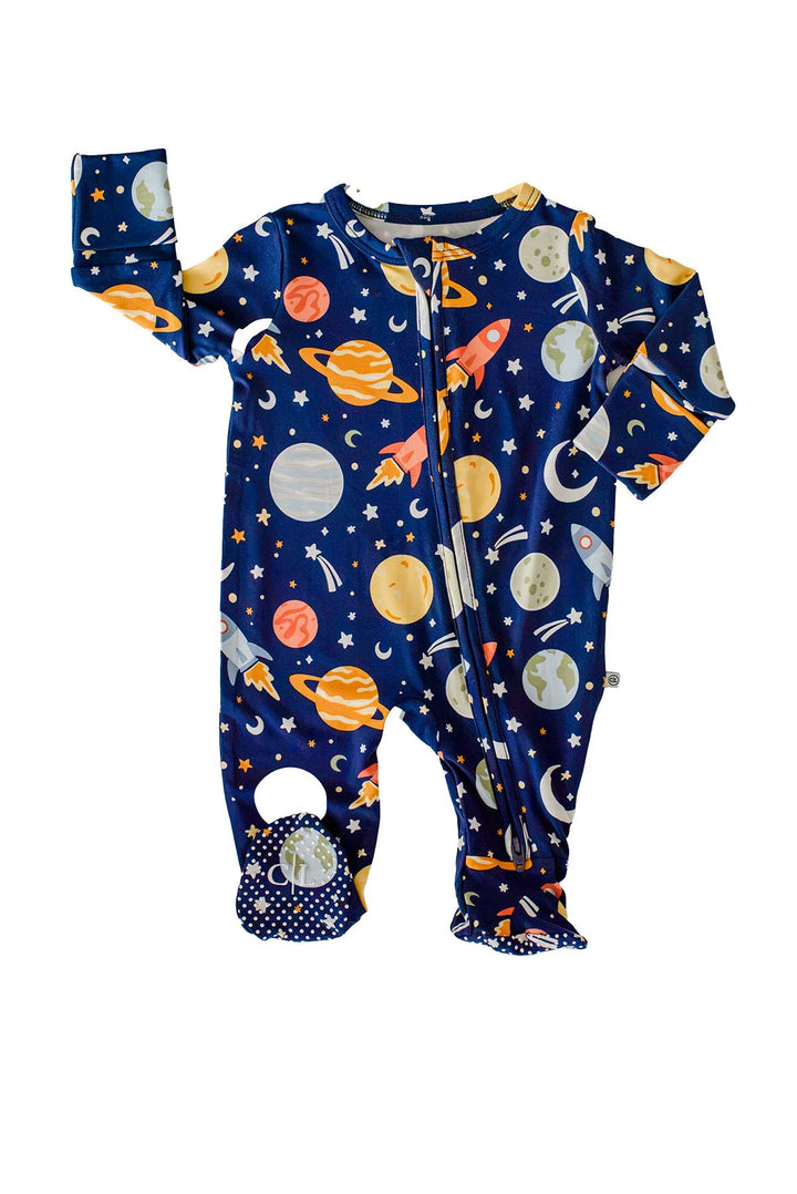 Flat lay of a Caden Lane navy bamboo glow-in-the-dark zipper footie in a Stellar Snuggles print featuring planets, rockets, moons, and stars, styled with one sleeve raised in a wave.