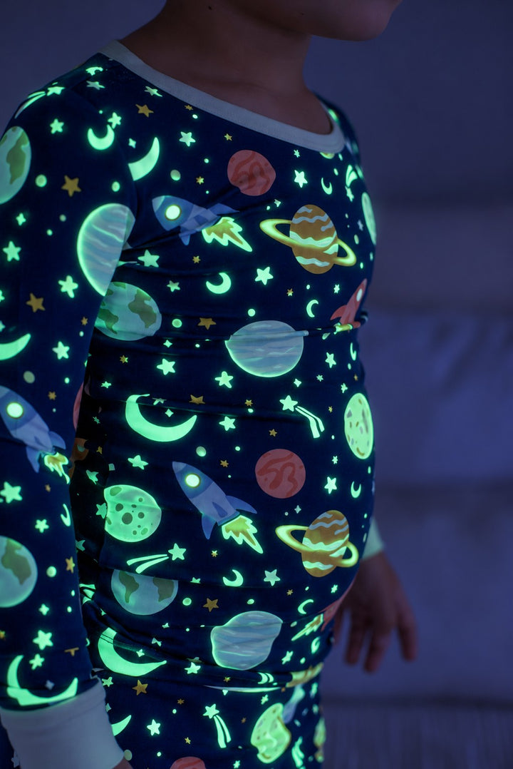 Close-up side view of a child wearing a glowing Caden Lane navy bamboo pajama top in a Stellar Snuggles print featuring rockets, ringed planets, and crescent moons.