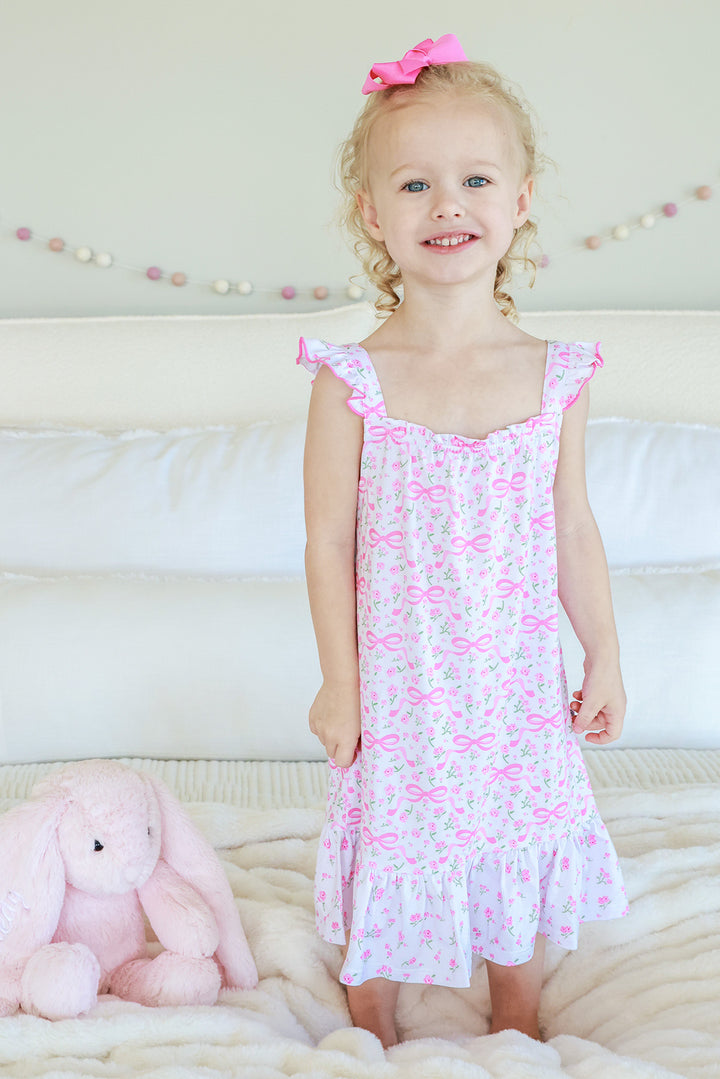 Young girl wearing Full Length Ruffle Nightgown in Dreamy Bows print, white background with pink bows pattern, flutter sleeves and ruffle hem