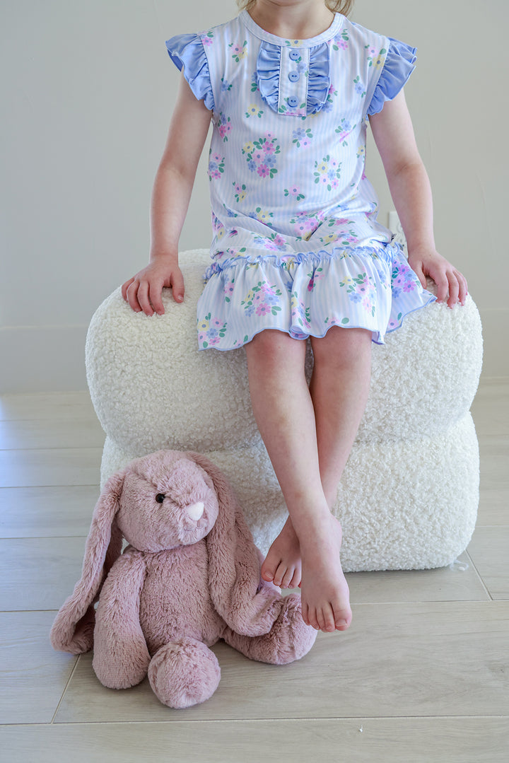 Young girl sitting on stool wearing Flutter Sleeve Nightgown in Heirloom Posies floral print with pink stuffed bunny at feet, full length view