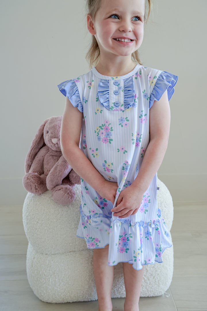 Young girl sitting on stool with stuffed bunny wearing Flutter Sleeve Nightgown in Heirloom Posies blue and white floral print, smiling full length view