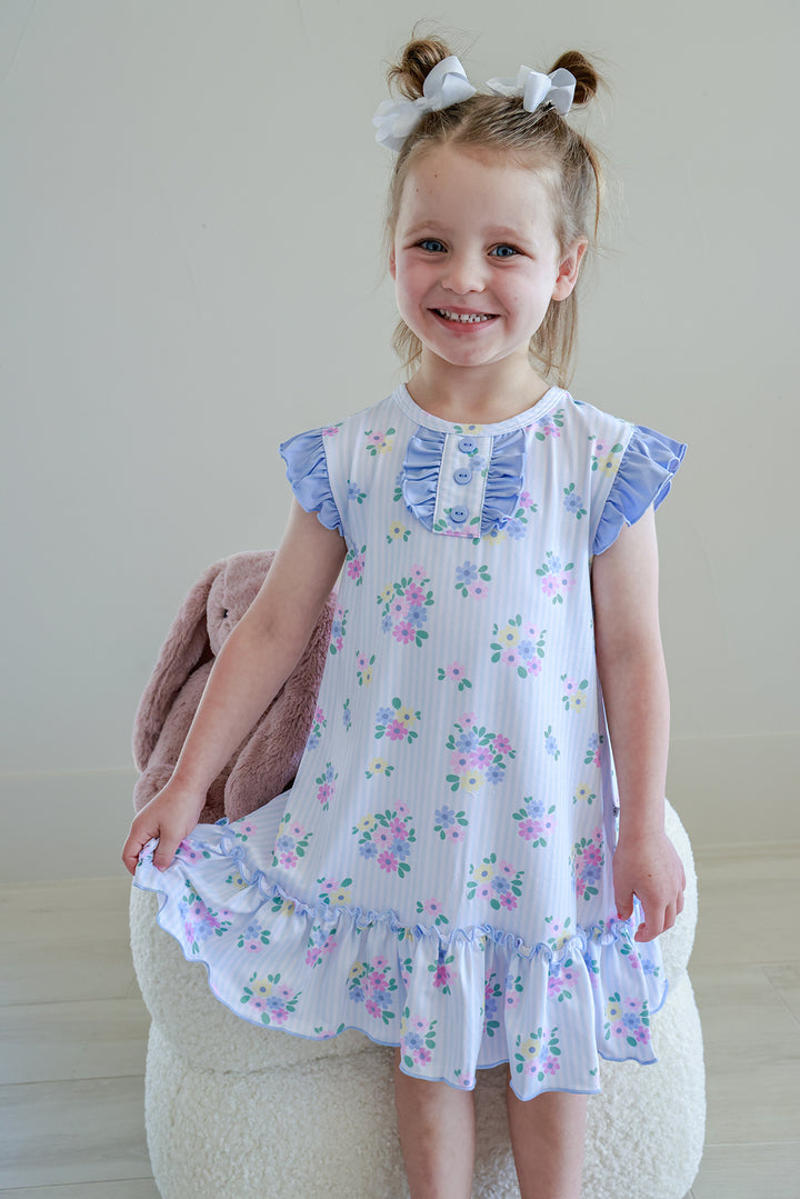 Young girl standing on stool wearing Flutter Sleeve Nightgown in Heirloom Posies blue and white floral print, full length front view with ruffle hem