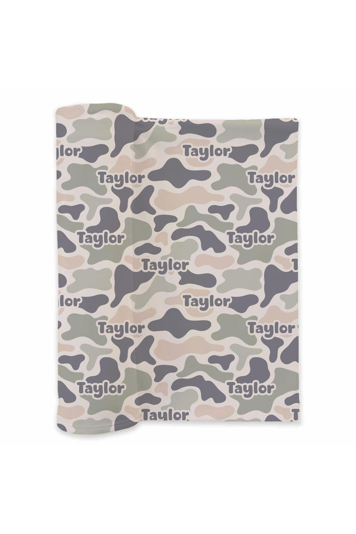 Mockup of personalized camo cutie swaddle blanket showing camo print in tan, olive, and gray with custom name repeated
