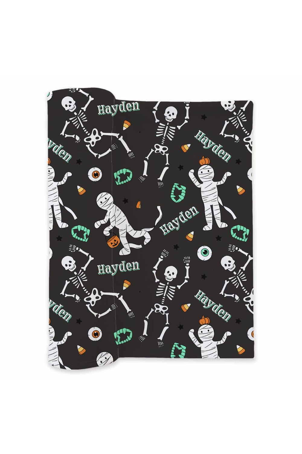 Folded black swaddle blanket personalized with the name 'Hayden' and printed with Halloween skeleton, mummy, candy corn, and pumpkin designs on a white background.