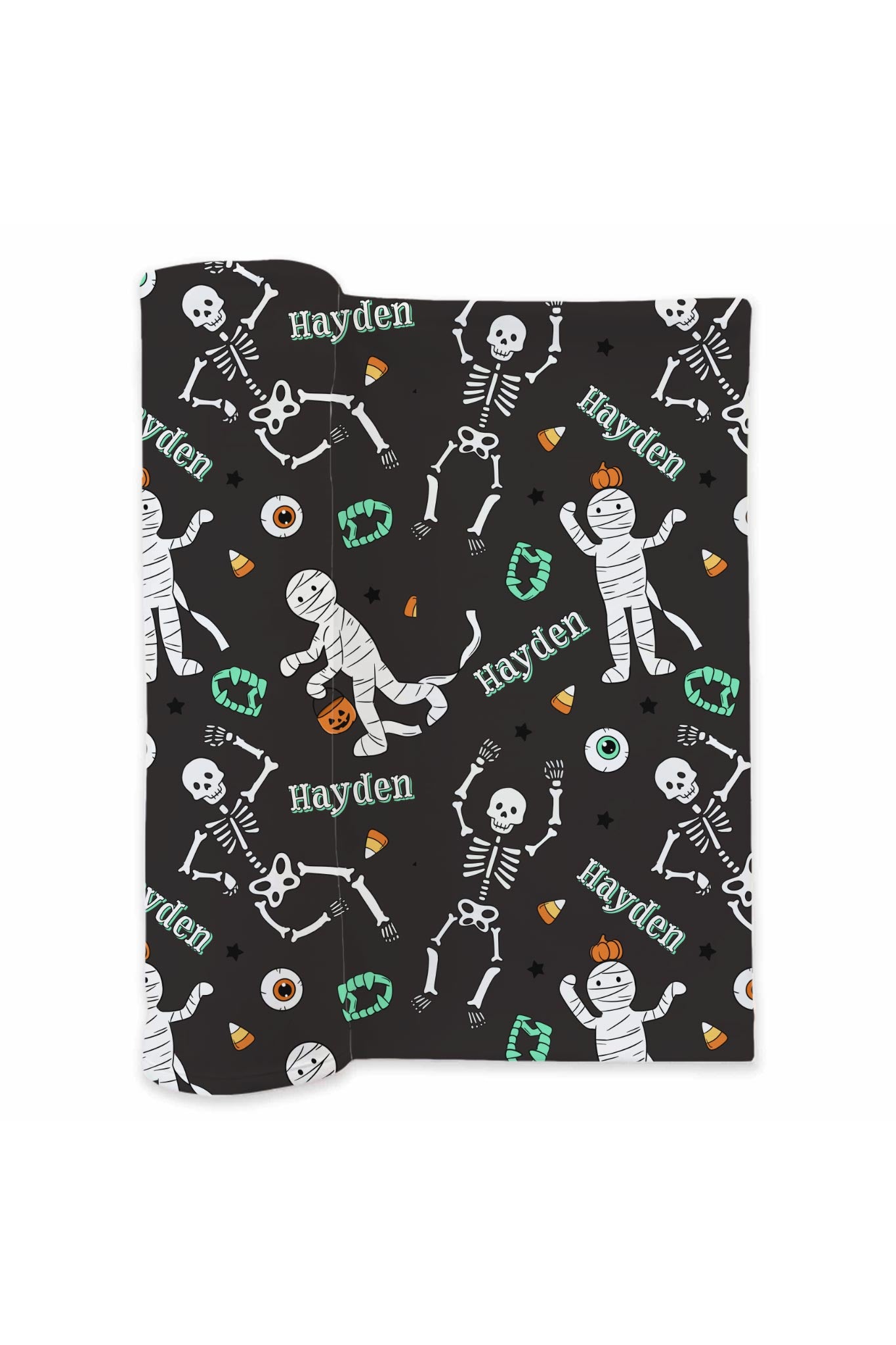 Folded black swaddle blanket personalized with the name 'Hayden' and printed with Halloween skeleton, mummy, candy corn, and pumpkin designs on a white background.