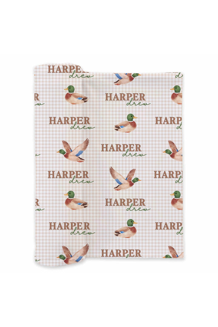 Flat lay of personalized little mallard duck print swaddle blanket showing full repeating name and flying duck pattern