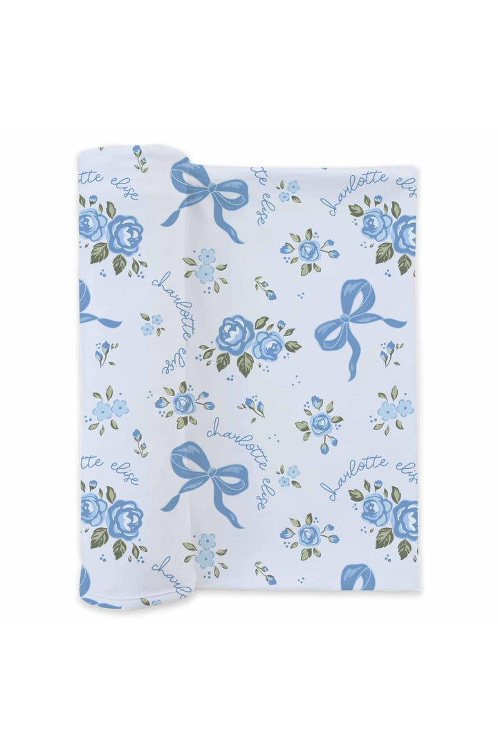 Rolled Tied In Blooms swaddle blanket with blue floral and bow print, personalized with names in cursive script
