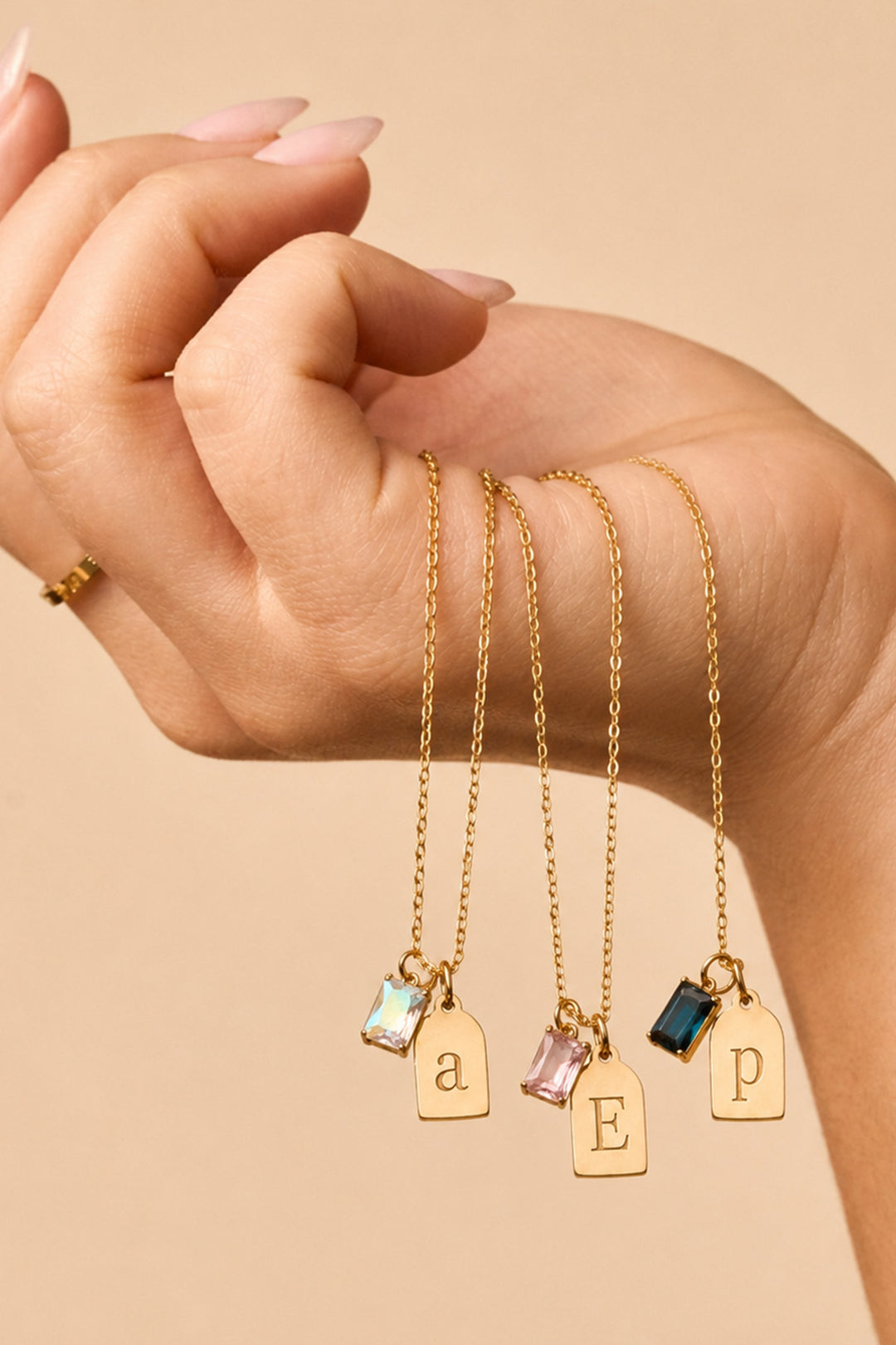 Caden Lane gold necklaces with initial tag charms "a," "E," and "p" paired with iridescent, pink, and blue birthstone charms, draped over wrist