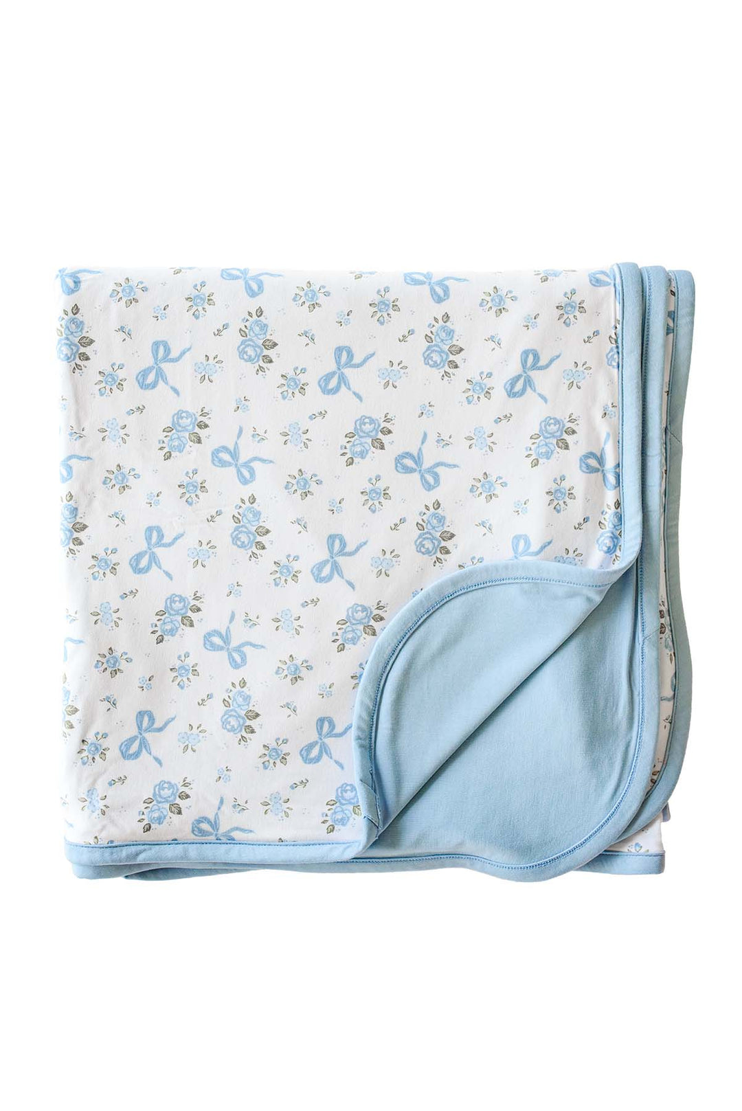 Flat lay of a Tied In Blooms double sided bamboo blanket with blue floral and bow print on one side and solid blue on the reverse, corner folded back