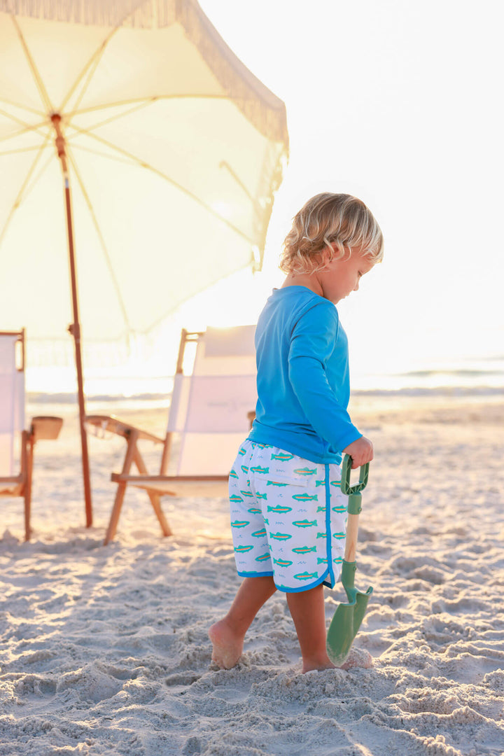 boy walking on beach in trout swim trunks with bright blue long sleeve rash guard shirt 