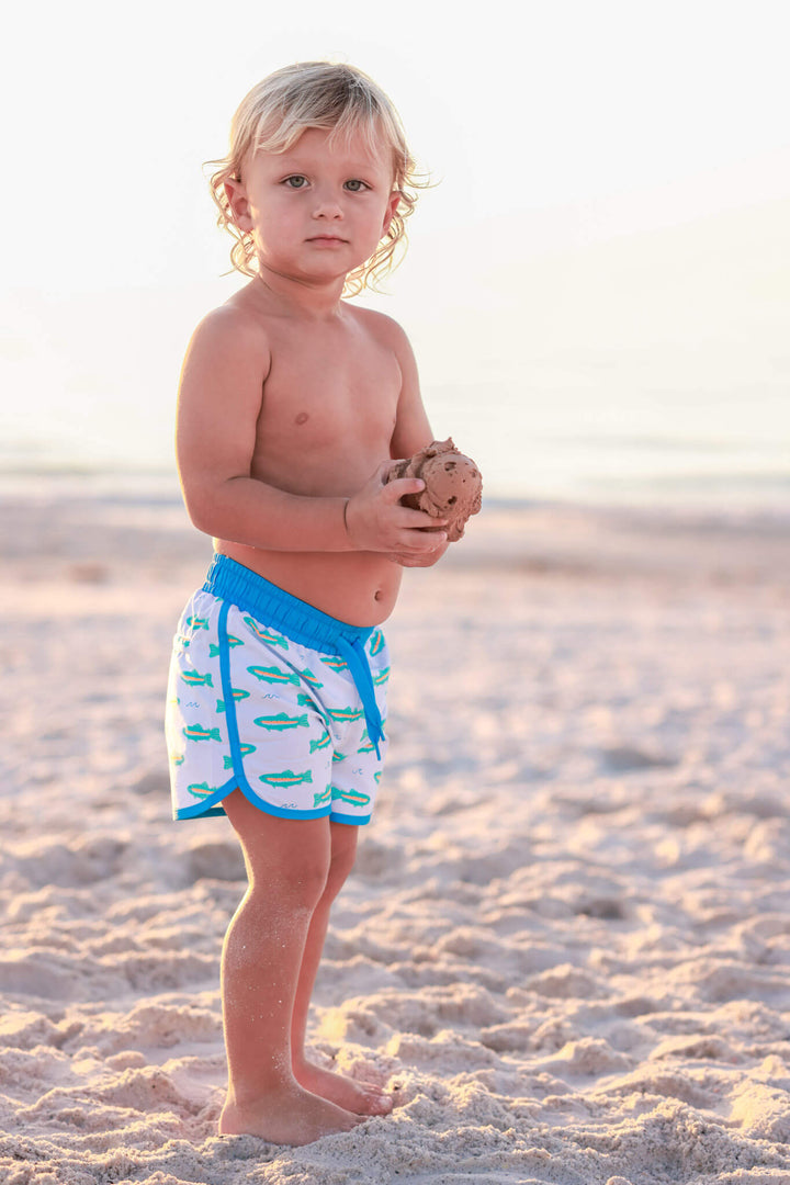 boy standing on beach in tiny trout swim trunks 