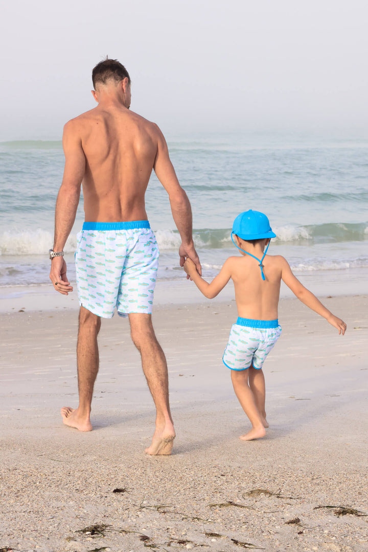 dad and son holding hands walking on beach in trout swim trunks 