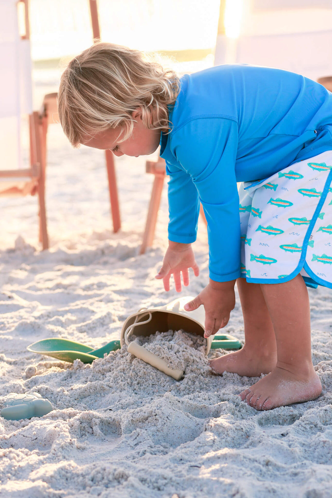 boy playing in sand in trout swim trunks and bright blue rash guard shirt 
