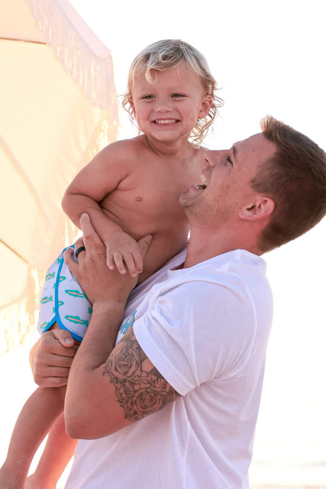 dad holding son on beach in trout swim trunks a white tshirt 