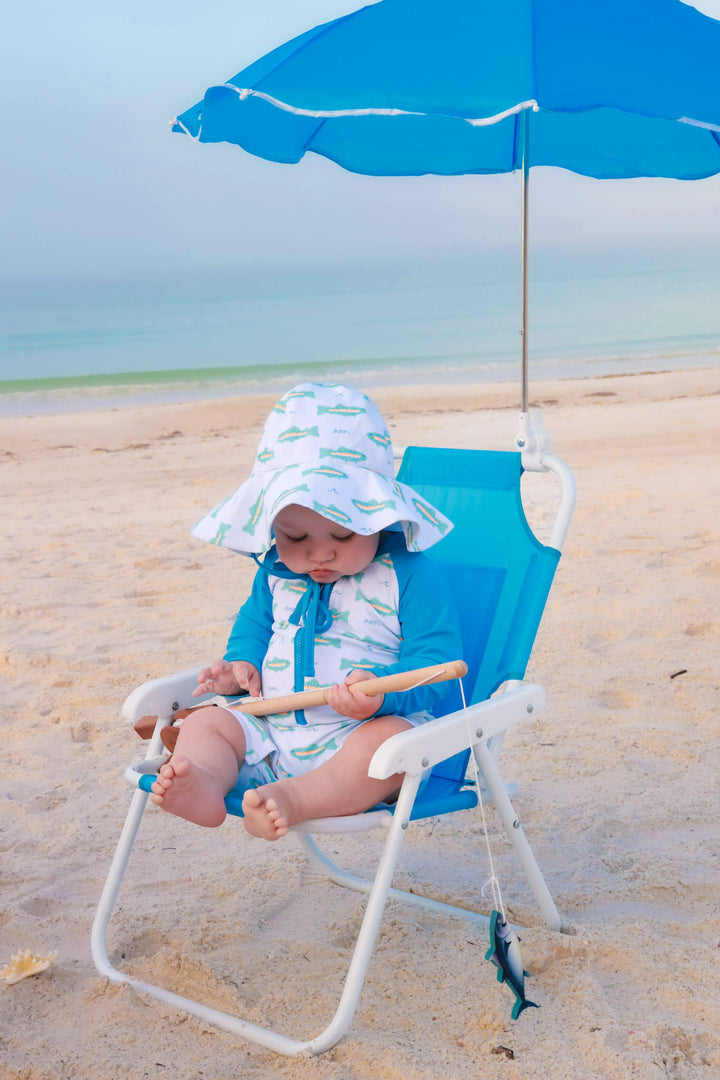 baby boy sitting on beach chair in tiny trout swim romper with matching sun hat 
