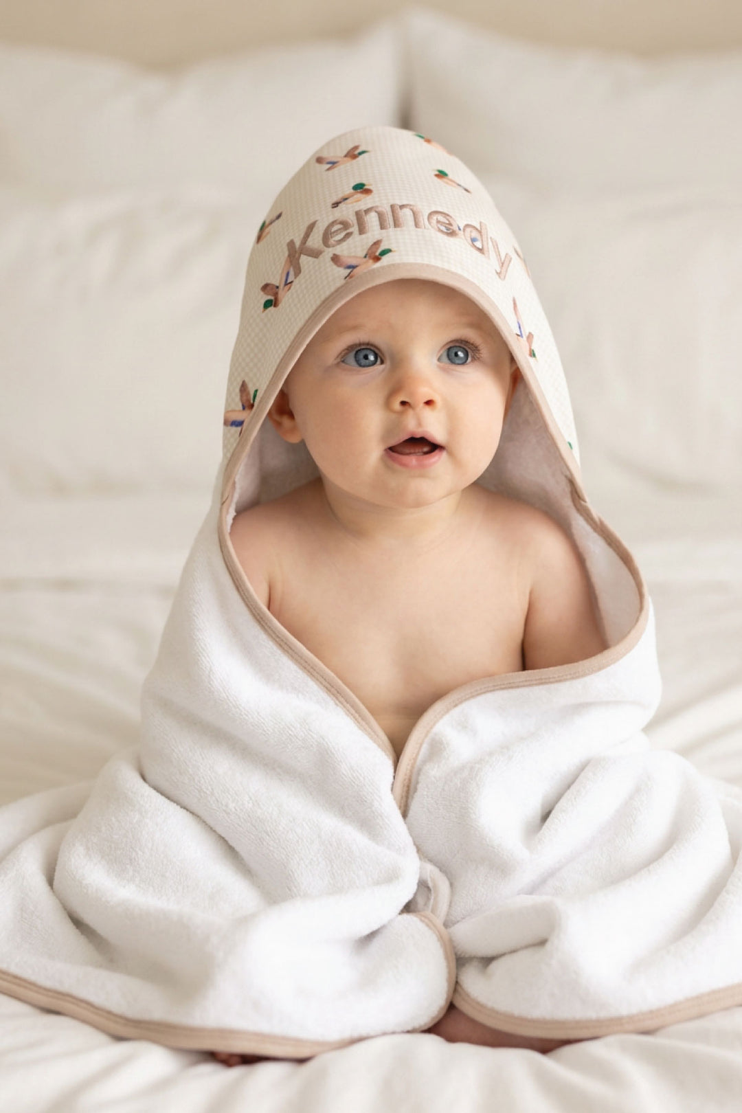 Baby looking forward wrapped in a personalized little mallard duck print bamboo hooded towel with name embroidered on hood, front-facing view