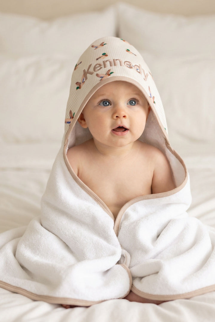 Baby looking forward wrapped in a personalized little mallard duck print bamboo hooded towel with name embroidered on hood, front-facing view