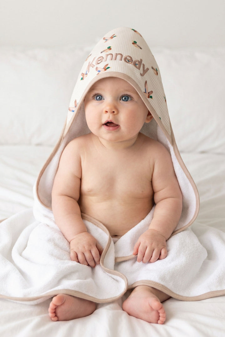 Baby sitting upright fully wrapped in a personalized little mallard duck print bamboo hooded towel with name embroidered on hood