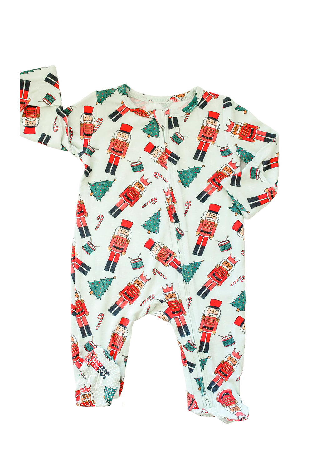 Flat lay of Caden Lane's white toy soldier print zip-up pajamas, featuring nutcrackers and Christmas trees, with patterned cuffs.